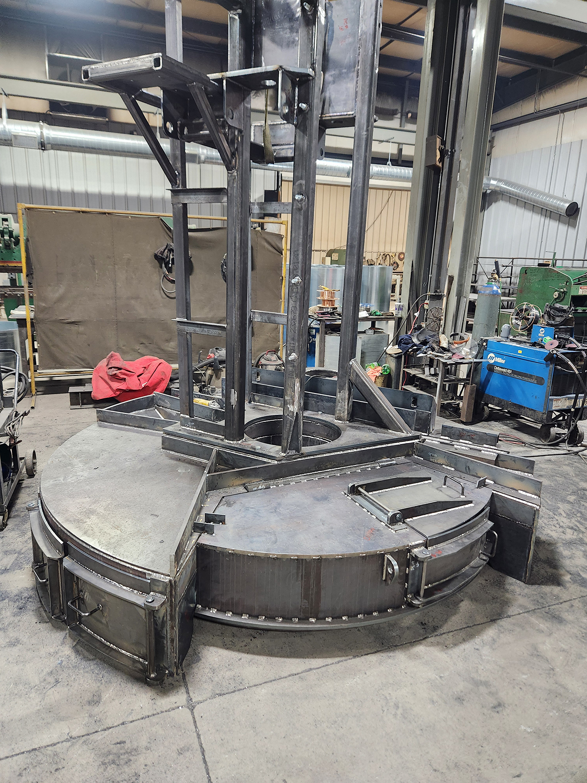 metalfab-004-new A complex, custom-fabricated heavy steel base and vertical support structure for industrial machinery, featuring precision welds and integrated access hatches, inside the Lee Industries workshop.
