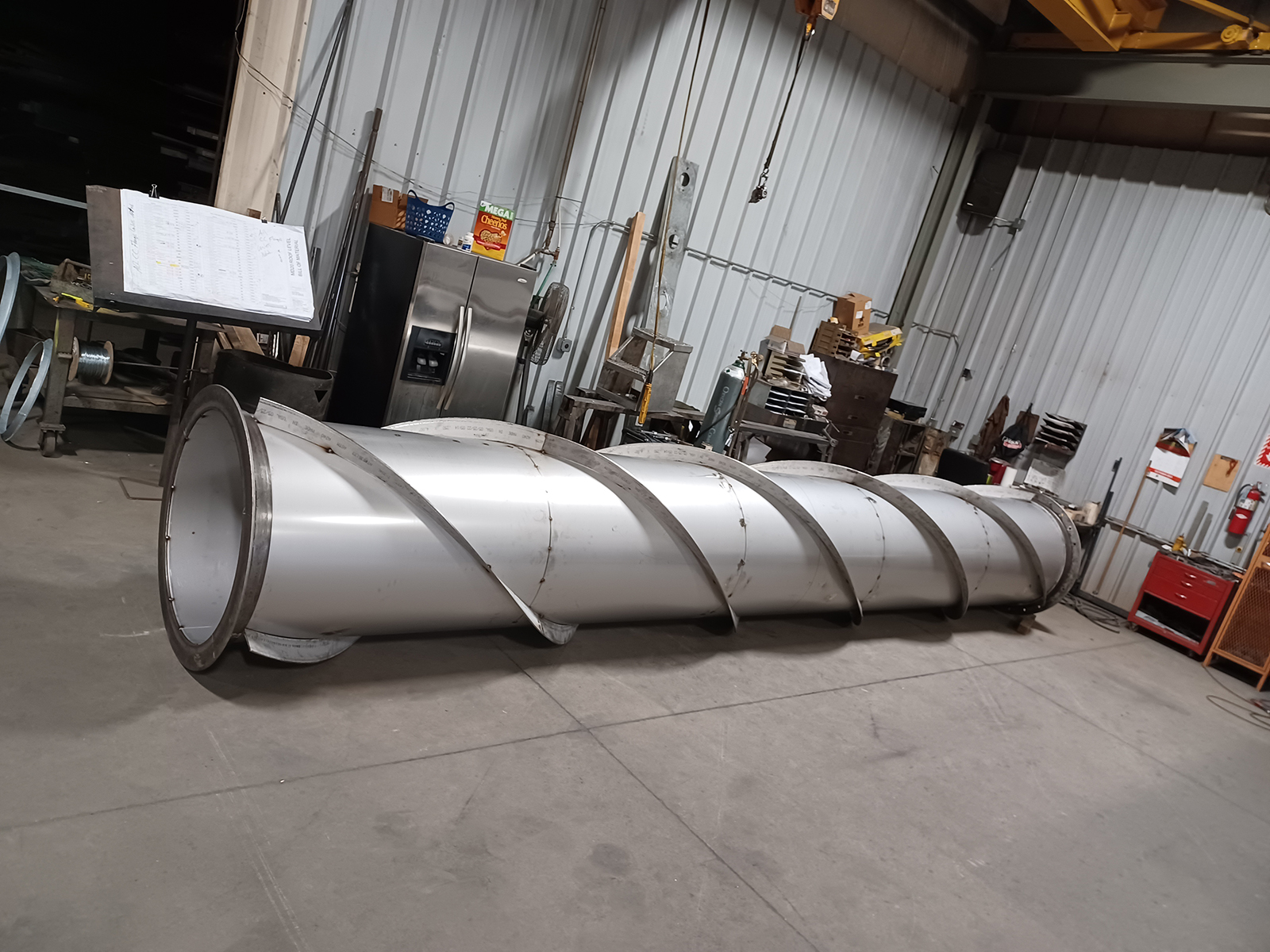 metalfab-005-new A custom-fabricated industrial screw conveyor with a large-diameter stainless steel auger and reinforced trough, staged for shipment at Lee Industries.